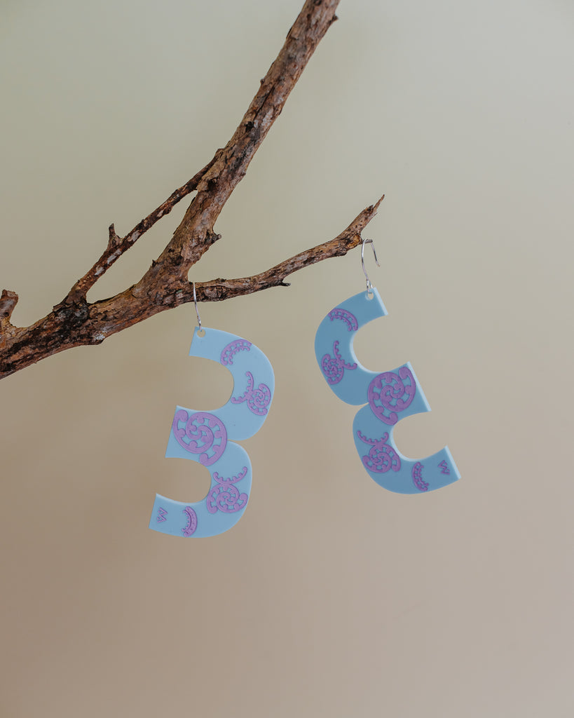 MISS MAIA, May 2022. The Blue and Lilac oversized Kōtuitui earrings sit perched and suspended from a branch.