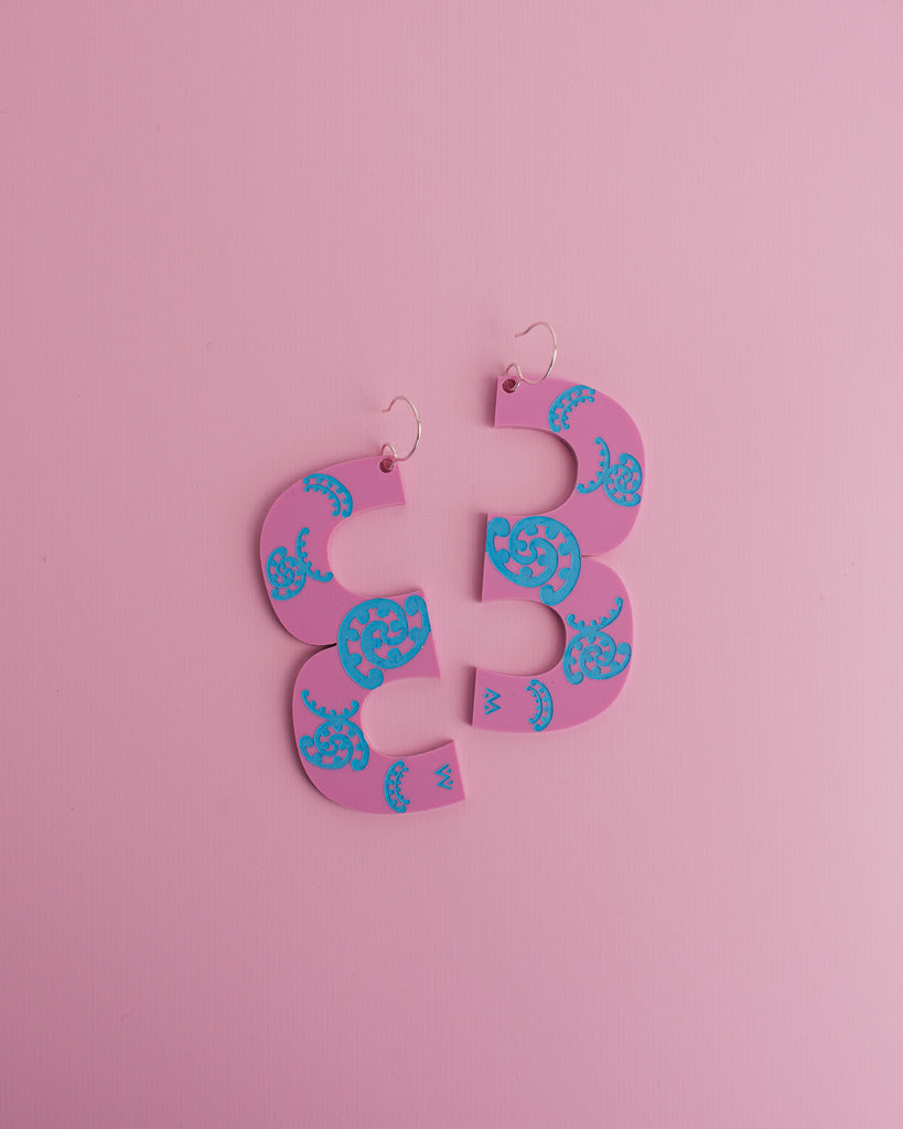 MISS MAIA, May 2022. A flat lay of the oversized Kōtuitui earrings in the Pink and Blue. They sit on a pink background.
