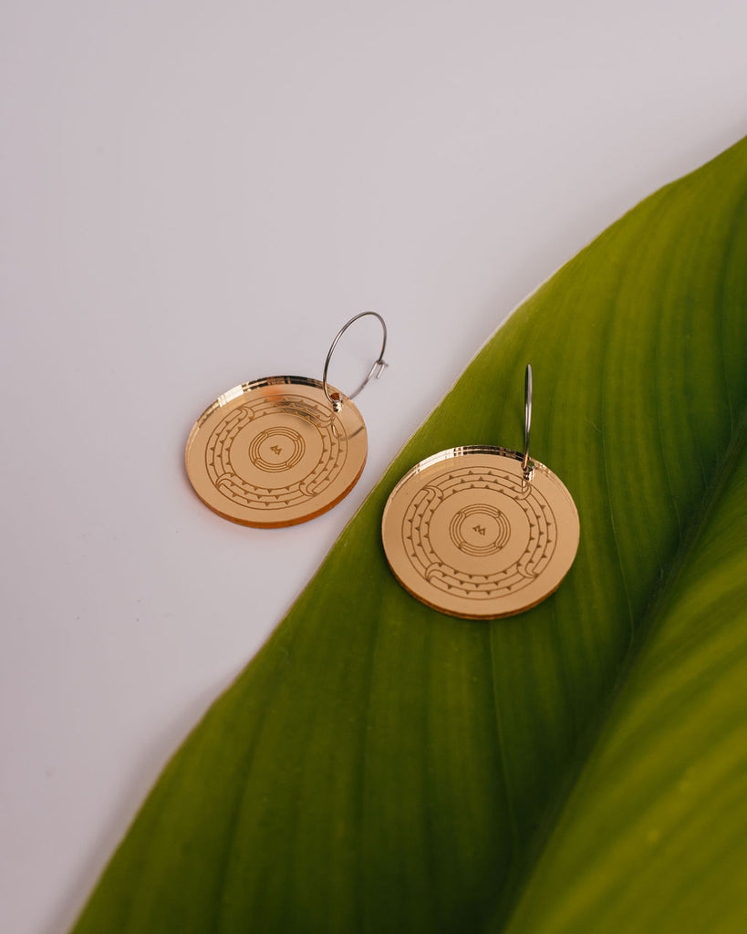 MISS MAIA, May 2022. The Turu earrings in Gold Mirror sit on a Green leaf with a white background.